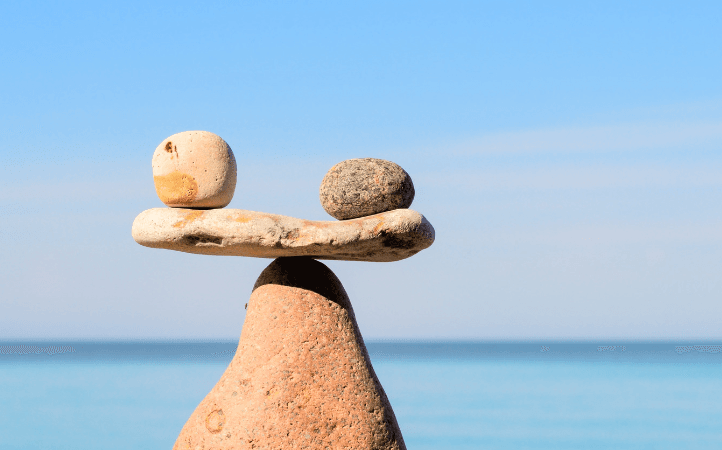 Balanced stones stacked near a calm sea with a clear blue sky in the background